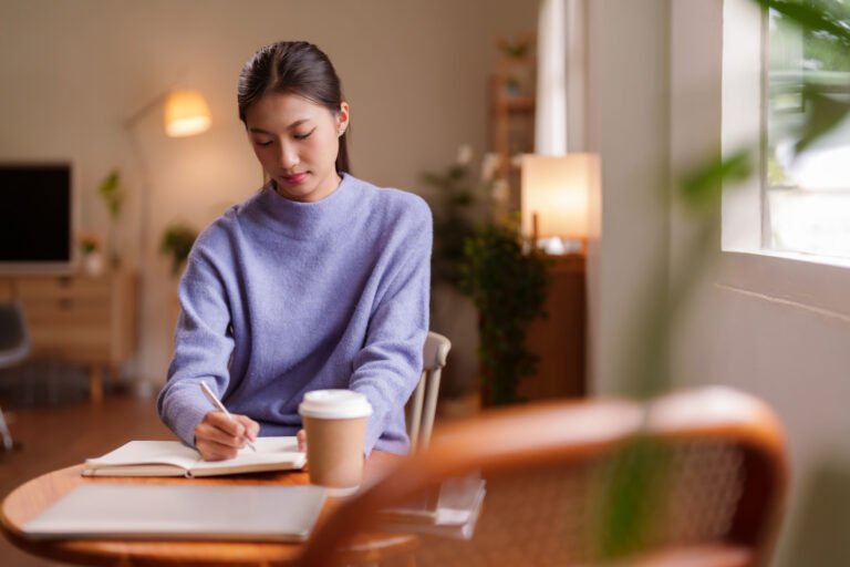 Asian young adult woman focused writing notes studying learning working from home cozy indoor comfortable space daily routine remote productivity