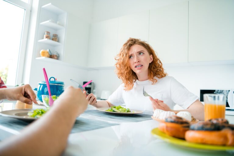 Young woman with red hair looking surprised while having meal in a bright kitchen during daylight