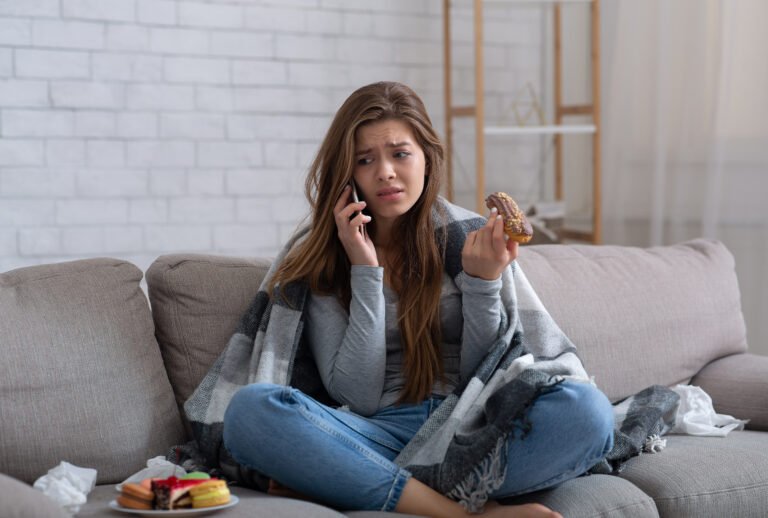 Depressed young lady with sweets talking on cellphone, having difficult conversation