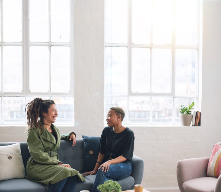 two woman friends talking having conversation sitting on sofa at home
