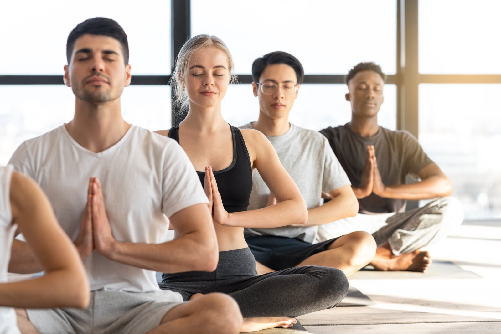 Meditation Exercise. Sporty Young People Practicing Yoga During Group Lesson In Studio