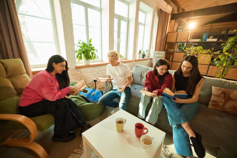 Group of young people sit with books and tea in loft living room enjoying literature and warm atmosphere.