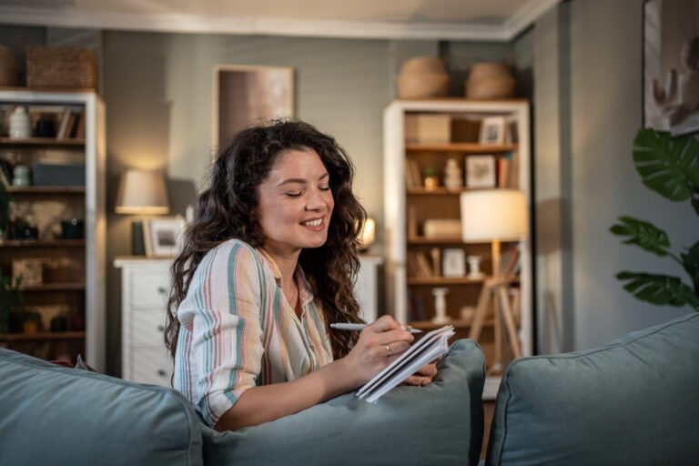 Young woman relaxing on sofa writing in notebook at home