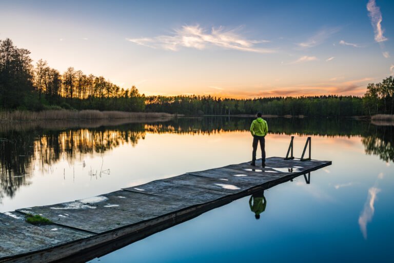 Man enjoys tranquility on a jetty at a still lake in Sweden during a vibrant sunset