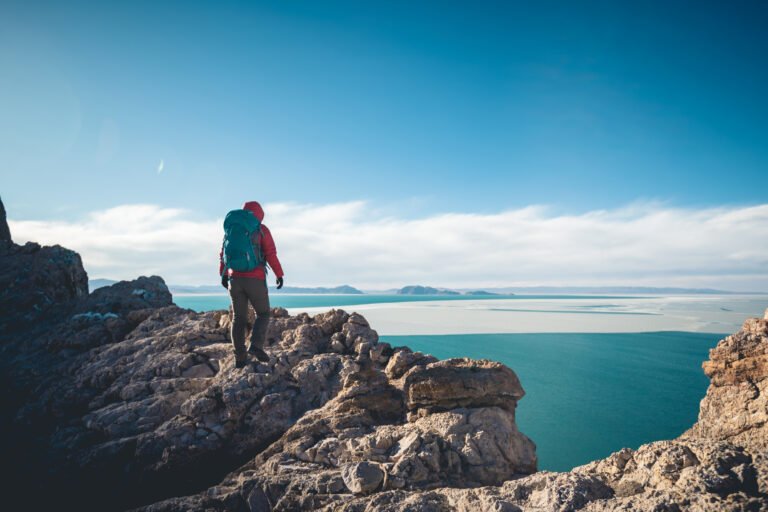 Woman hiker climbing to mountain top cliff edge at lakeside