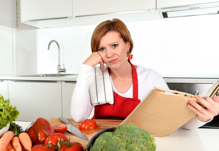 tired cook woman bored in kitchen reading recipes book