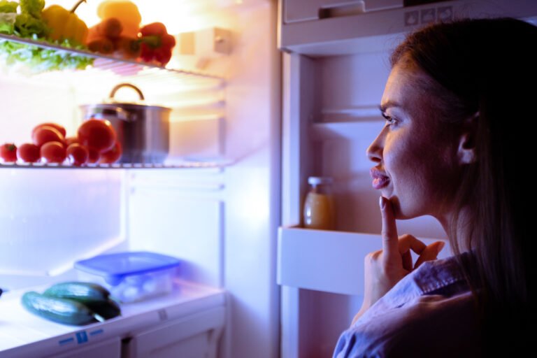 Pensive girl looking into refrigerator for late snack