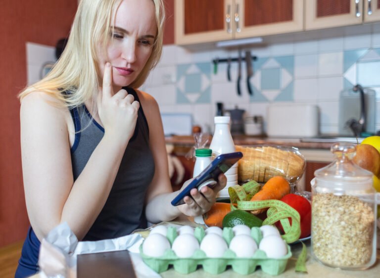 A woman checks the calorie content of food in a smartphone app. Calorie counting for weight loss. There are products for dieting on the table