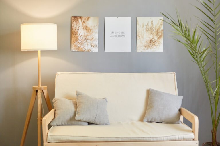 Cozy living room with gray decorated with pictures, green flower and lamp, stylish sofa with pillows.