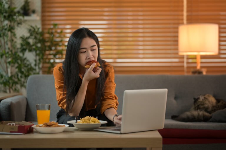 Pretty young woman eating a piece of pizza and watching movie on laptop. Takeaway, fast food and domestic life.