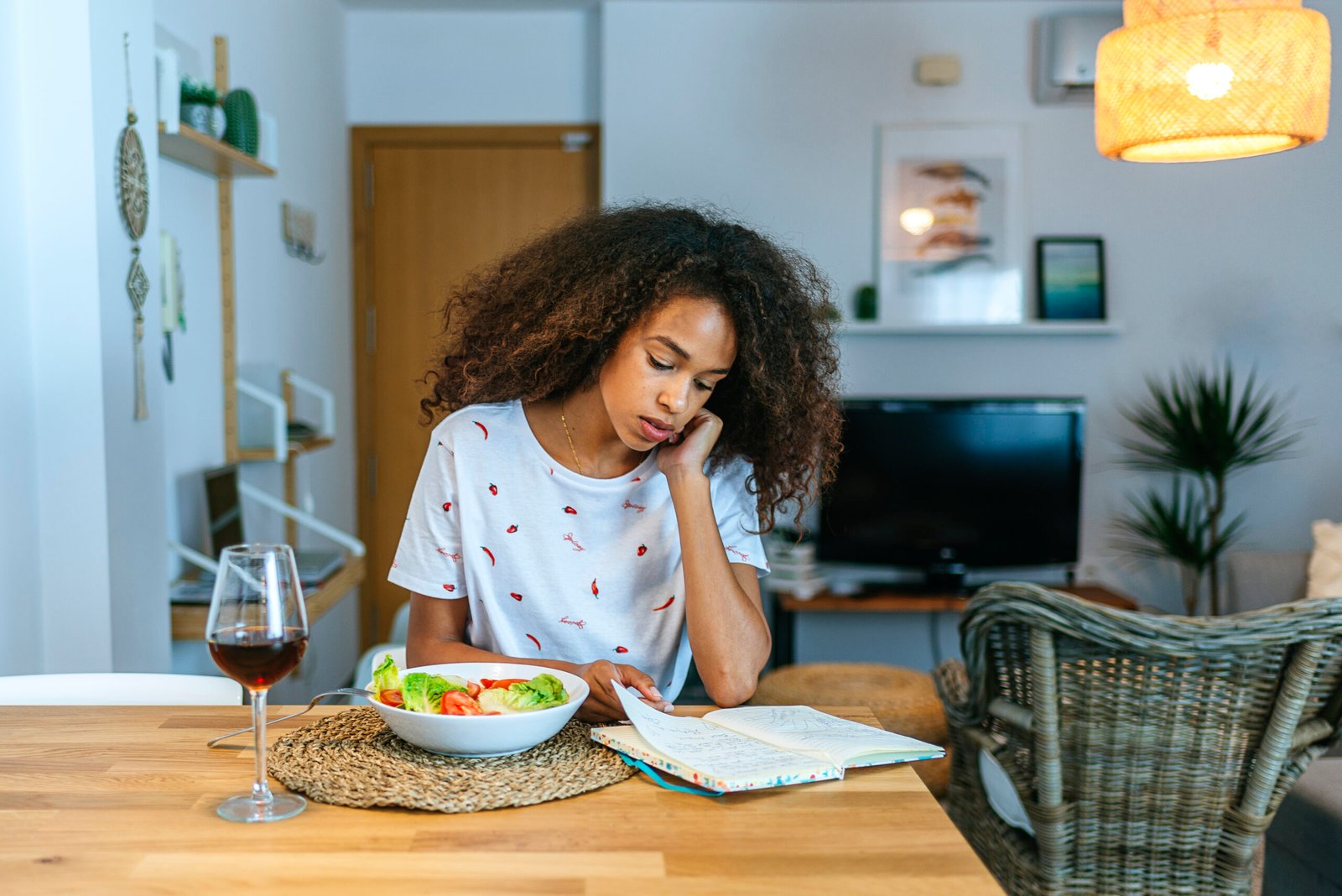 Woman at home reading notebook and eating salad and wine