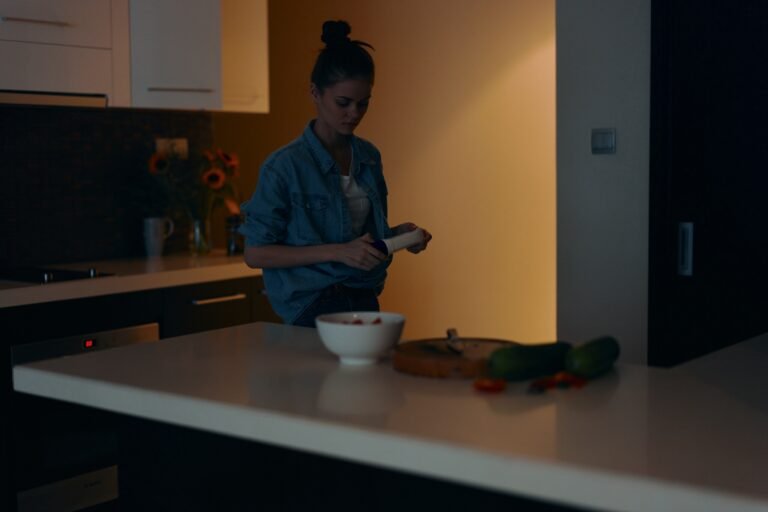 Beautiful young woman holding a mobile phone and enjoying a healthy meal in a cozy kitchen interior.