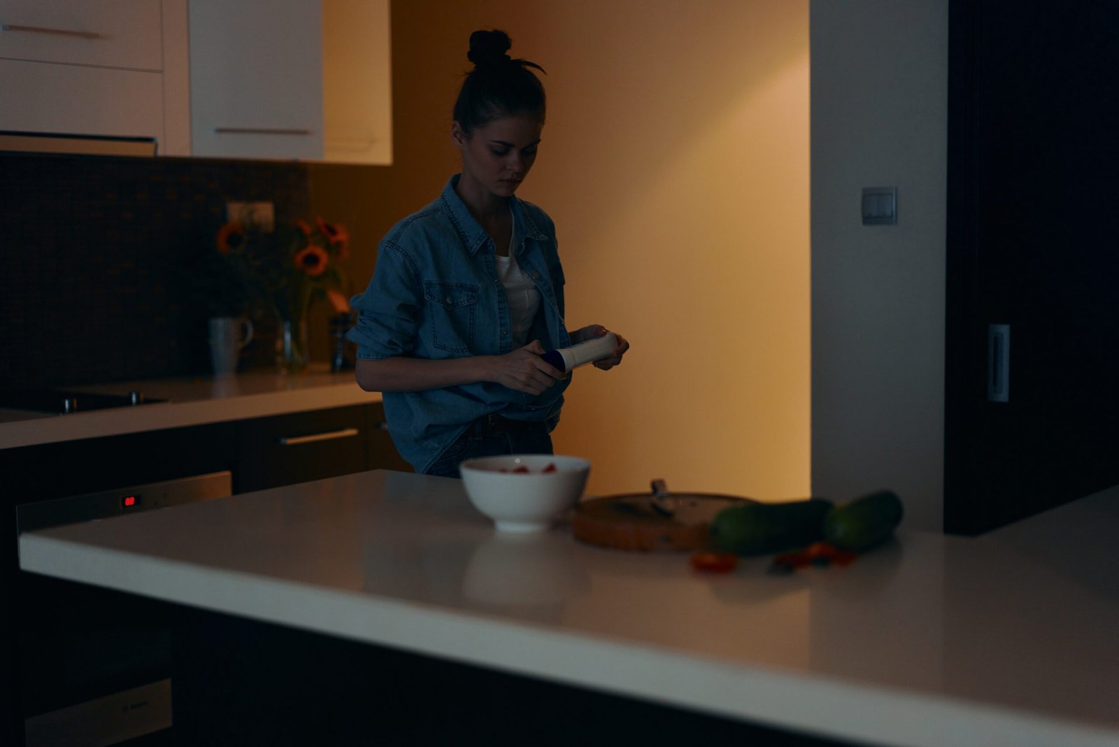 Beautiful young woman holding a mobile phone and enjoying a healthy meal in a cozy kitchen interior.
