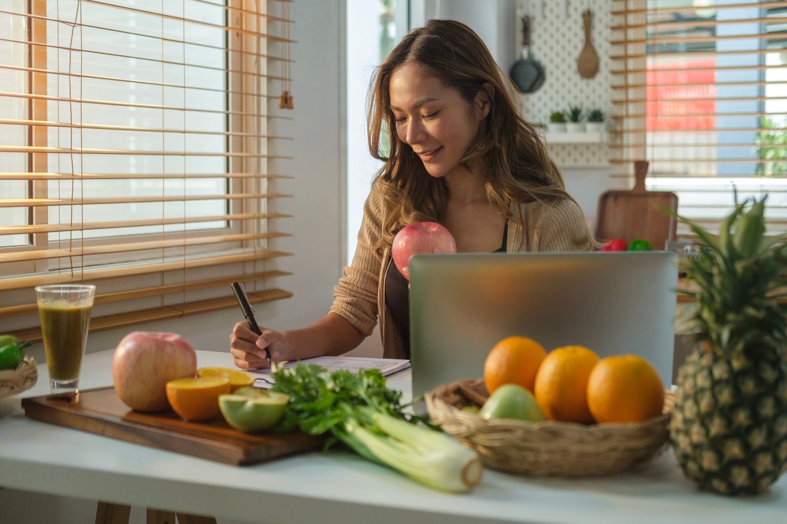 Beautiful young woman sitting in kitchen and writing down healthy recipe or daily ration diet. Healthy lifestyle concept.