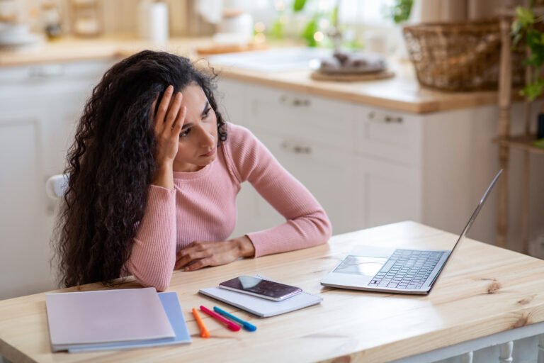 Bored Freelancer Lady Sitting At Table With Laptop In Kitchen