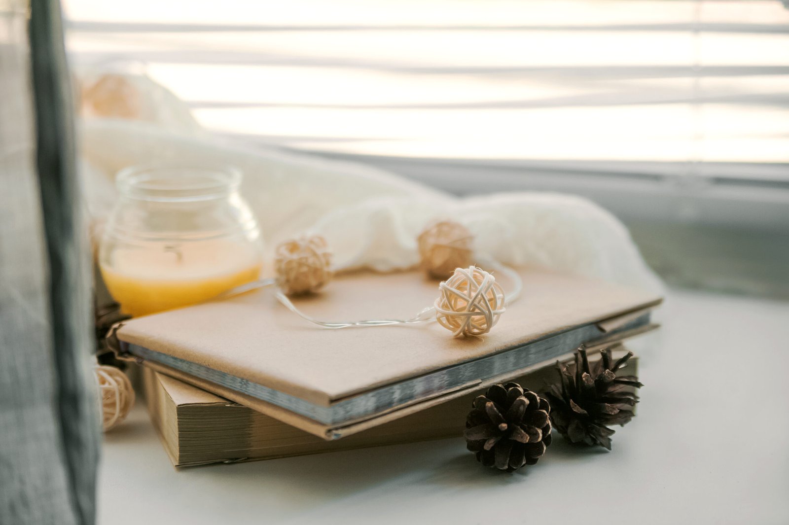 Burning candles and white sweaters on windowsill. Cozy autumn and winter concept, window with blinds...