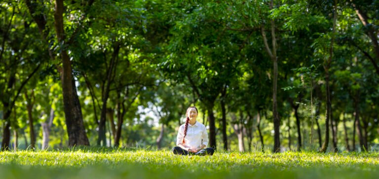 Woman relaxingly practicing meditation in the forest to attain happiness from inner peace wisdom with beam of sun light for healthy mind and soul concept