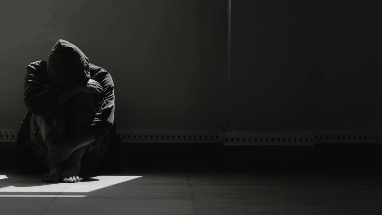 hopeless man sitting alone with hugging his knees on the floor in empty dark room