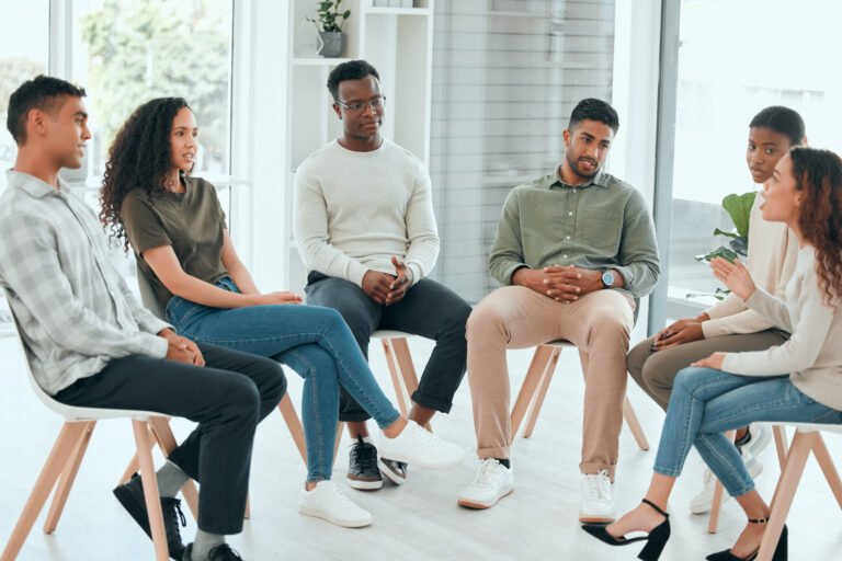 Shot of a diverse group of people sitting together and talking during group therapy