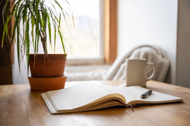 An open journal and pen on a table with a cup of tea for a mental health break.