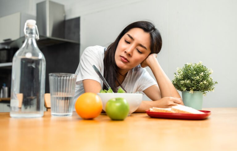 Unhappy female looking to organic greens vegetable salad in weight loss diet and wellness on table. Tired woman dislike eat bored with food healthy salad breakfast in kitchen. Diet food concept.